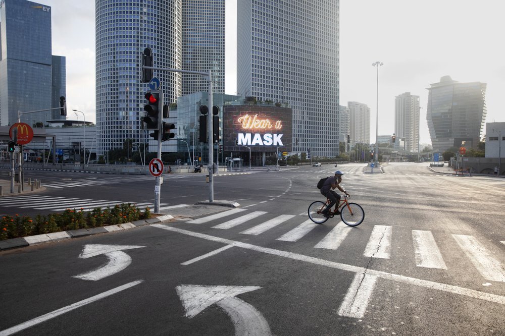 A man rides a bicycle next to a billboard calling people to wear masks, on empty road following new restrictions in the three-week nationwide lockdown, in Tel Aviv 