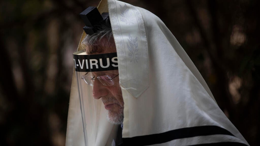 An ultra-Orthodox Jewish man wears a face mask during a morning prayer next to his house as synagogues are limited to twenty people due to the coronavirus pandemic, in Bnei Brak 