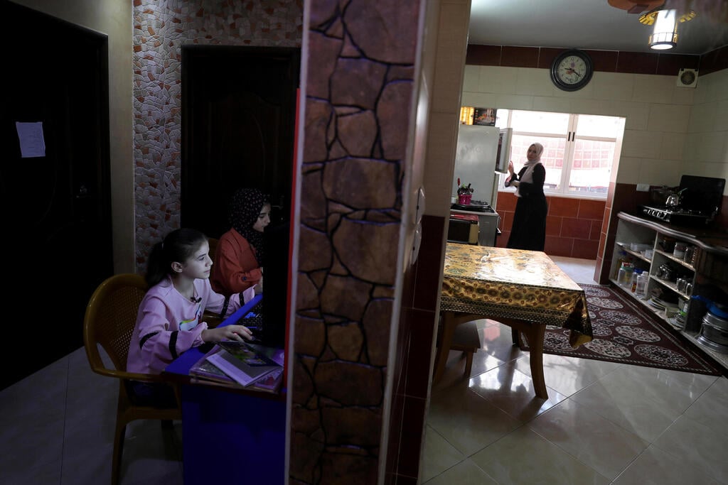 Palestinian sisters Raseel and Mariam Hussein attend their online lessons as their mother Yasmine works in their home kitchen, amid the coronavirus disease (COVID-19) outbreak, in Gaza City 