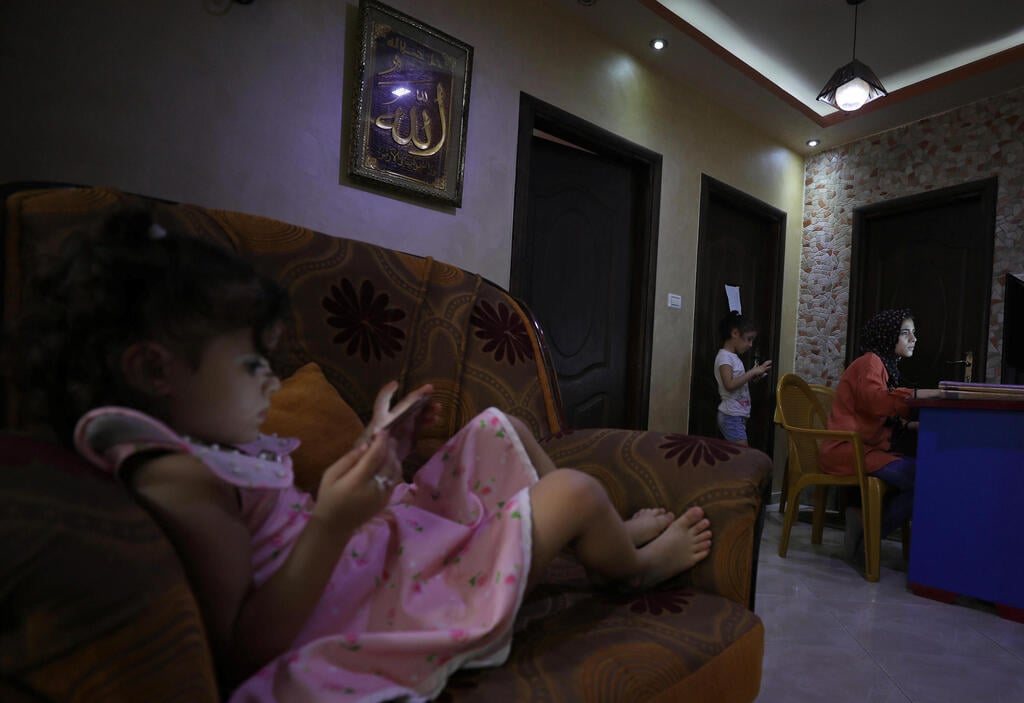 Palestinian student Raseel Hussein attends an online lesson as her sisters play with mobile phones in their family home, amid the coronavirus disease (COVID-19) outbreak, in Gaza City 