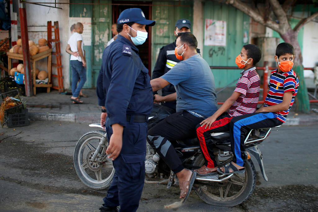 A Palestinian man with his children wearing protective face masks rides his motorcycle by police officers amid the coronavirus disease (COVID-19) outbreak, in the northern Gaza Strip 