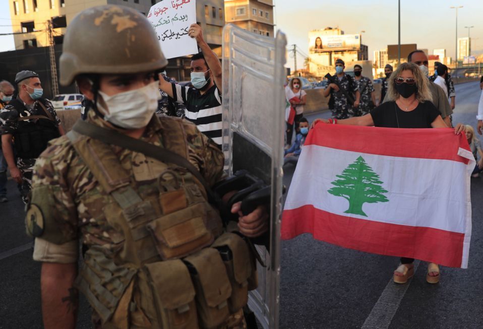 A Lebanese army soldier passes in front of an anti-government protester holding a national flag and blocking a main highway that links Beirut with north Lebanon during a protest against rising prices and worsening economic and financial conditions 