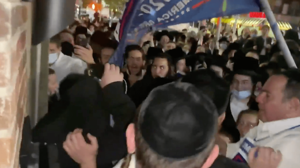 Jacob Kornbluh, a reporter and a member of the Hasidic community in Borough Park, surrounded by a large crowd led by Heshy Tischler, a local figure who has become a leader of the movement to defy Covid restrictions