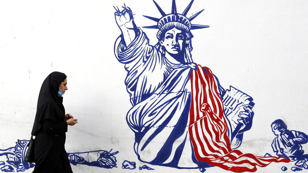 An Iranian woman walk past a mural depicting a defaced Statue of Liberty on the wall of former US embassy in Tehran, Iran