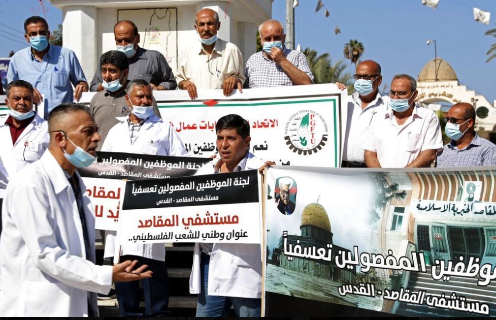 Medical workers wear face masks and hold placards while staging a sit-in protest at the Unknown Soldier Square in Gaza City, Arabic sign reads: "Firing us is a death sentence on our profession and families"