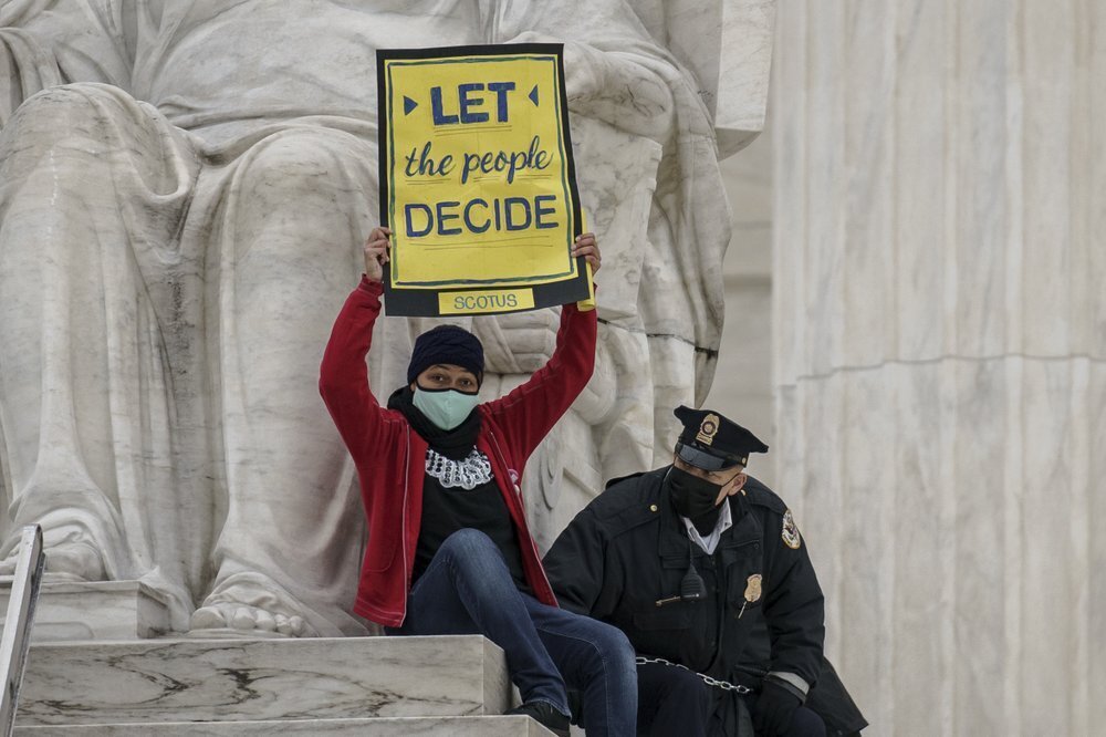 A protester opposed to the Senate's race to confirm Amy Coney Barrett is removed by police after chaining themselves to a railing and holding a sign while sitting atop the statue Contemplation of Justice, at the Supreme Court building in Washington 