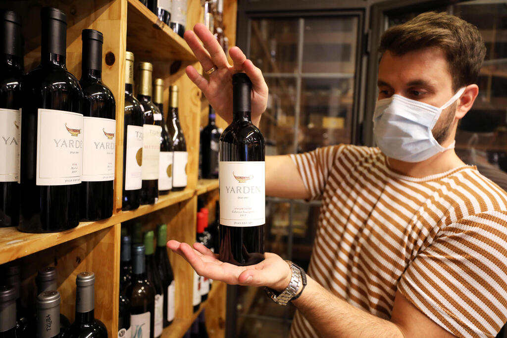  shop owner holds a bottle of wine from the Golan Heights Winery 