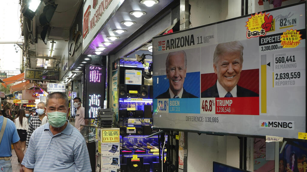 A man walks past a TV monitor showing a news program reporting the U.S. presidential election between President Donald Trump, right, and former Vice President Joe Biden, left, in Hong Kong