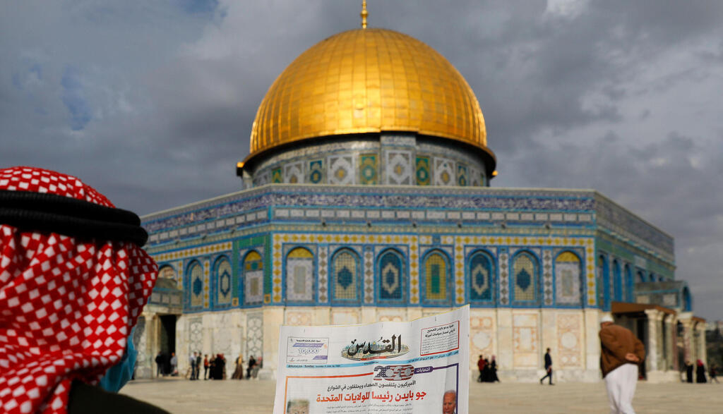 A Palestinian man reads the front page of Al-Quds newspaper, headlined in Arabic "Joe Biden the new US President" in front of the Dome of the Rock in the al-Aqsa mosque compound