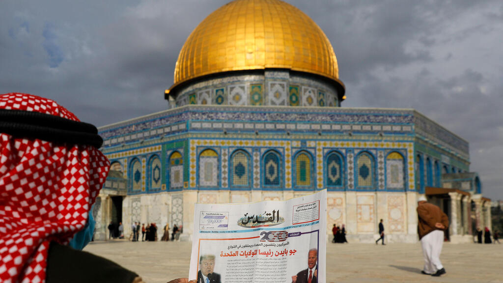 A Palestinian man reads the front page of Al-Quds newspaper, headlined in Arabic "Joe Biden the new US President" in front of the Dome of the Rock in the al-Aqsa mosque compound