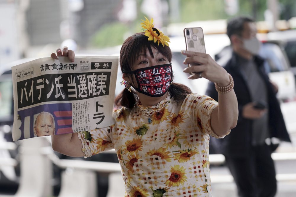 A passer-by takes a selfie with an extra newspaper reporting on President-elect Joe Biden's win in the U.S. presidential election, in Tokyo; headline reads: “Mr. Biden Assured to win.” 