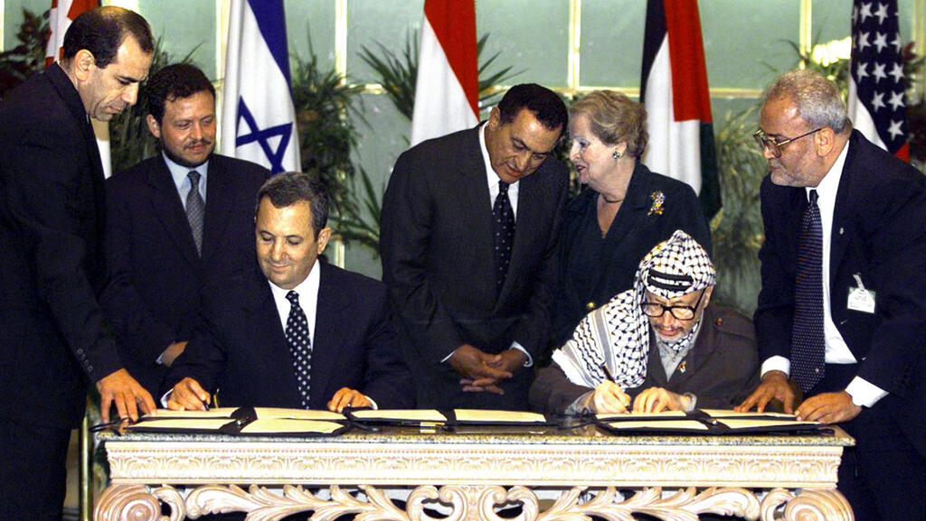 Saeb Erekat, right, watches as then-Prime Minister Ehud Barak and Palestinian leader Yasser Arafat sign an agreement paving the way for talks on a permanent peace settlement, Sept. 1999 