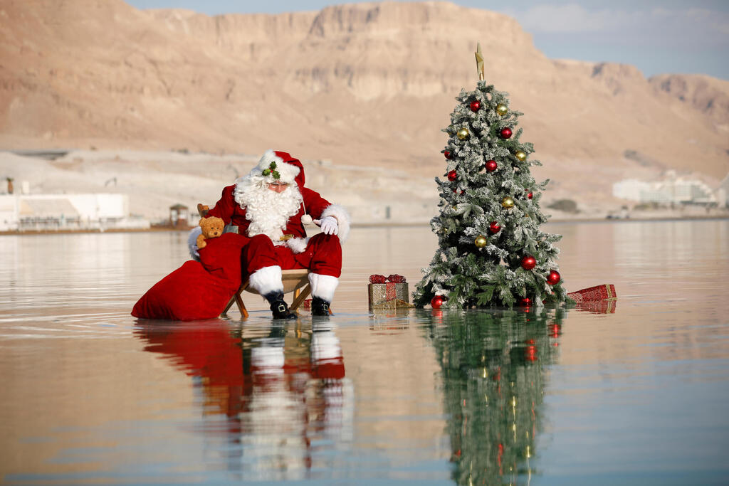 Issa Kassissieh, wearing a Santa Claus costume, looks on as he poses for a picture while sitting next to a Christmas tree on a salt formation in the Dead Sea 
