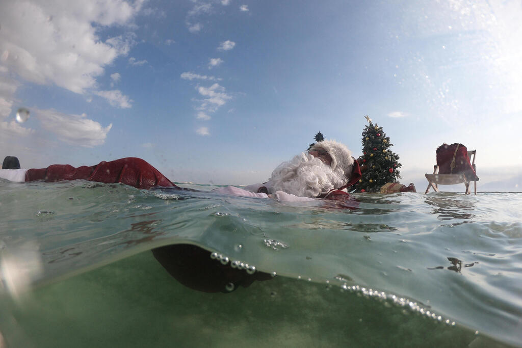 Issa Kassissieh, dressed as Santa Claus, waves next to a Christmas tree erected on a salt formation during filming for a Christmas greeting video from the Holy Land in the Dead Sea near Ein Bokeq, Israel 