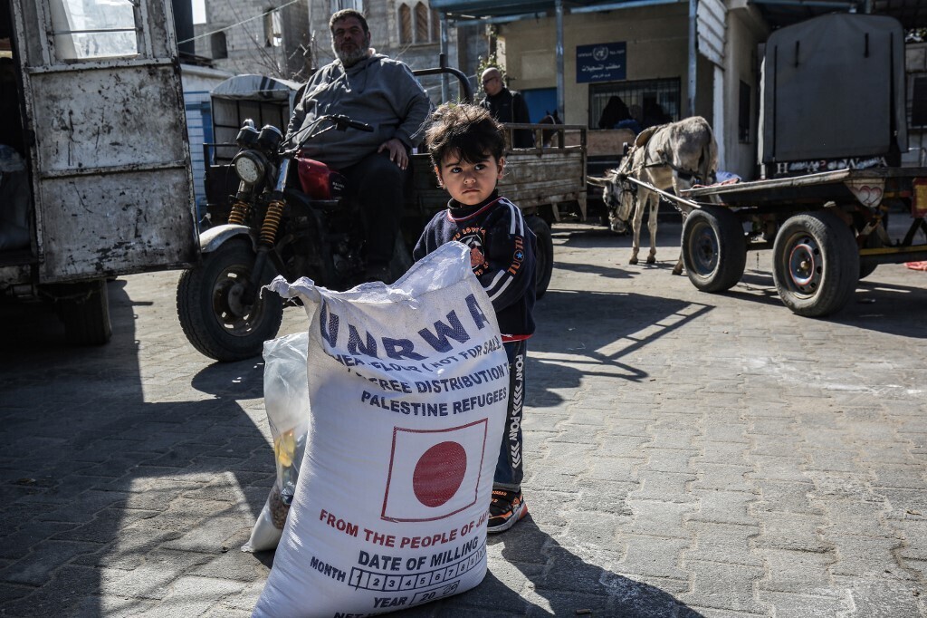 a child stands next to a sack of flour as people come to receive food aid from a United Nations Relief and Works Agency (UNRWA) distribution center in Khan Younis in the Gaza Strip 