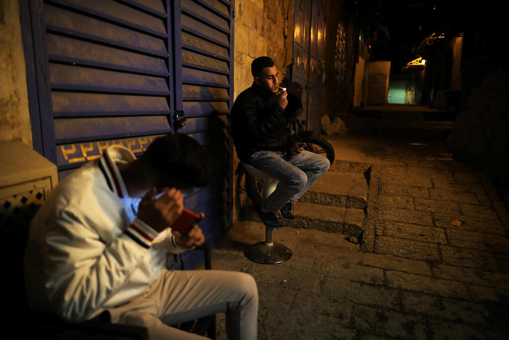 Palestinian youth smokes as another uses his mobile phone in an alley at night in Jerusalem's Old City amid coronavirus crisis 