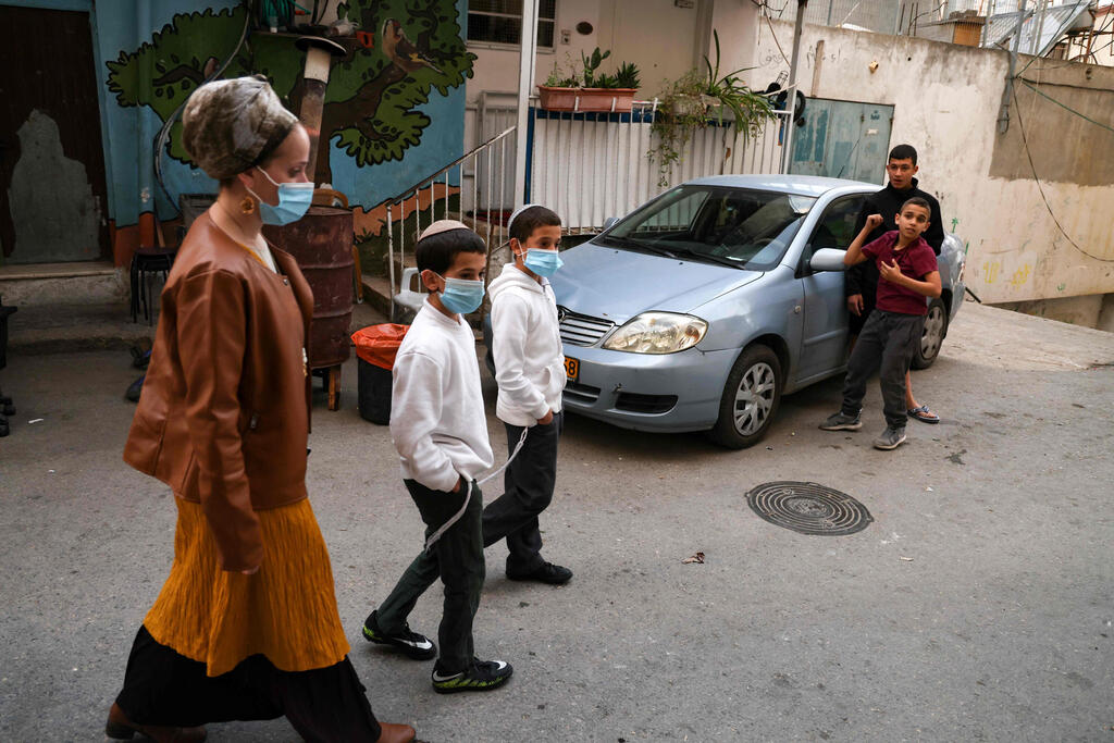 Arab children look on as Nira Rabinowicz (L) walks with two of her children in a street in Silwan