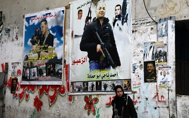 A Palestinian woman stands against a wall plastered with posters picturing “martyrs,” at a market in the Balata camp, near the West Bank city of Nablus 