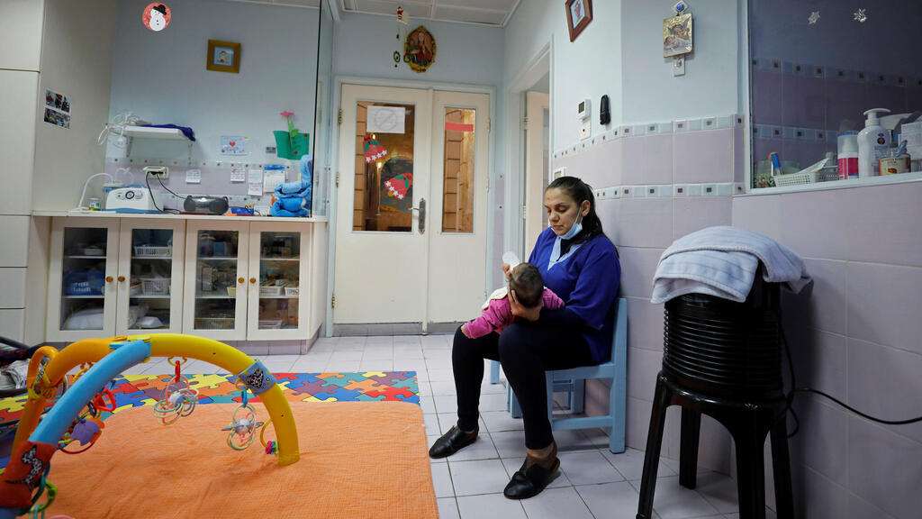 staff member feeds an infant at The Creche, a house sheltering children, in Bethlehem
