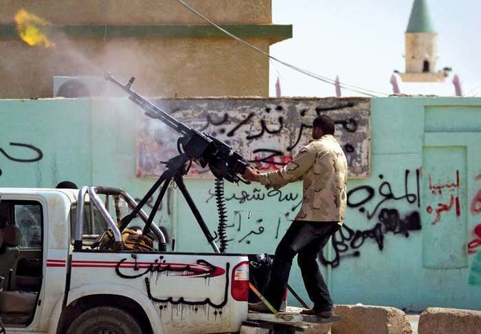 A rebel firing a gun in the heavily contested city of Ajdābiyā in eastern Libya, March 6, 2011. The graffiti on the side of the truck reads, “Army of Libya"