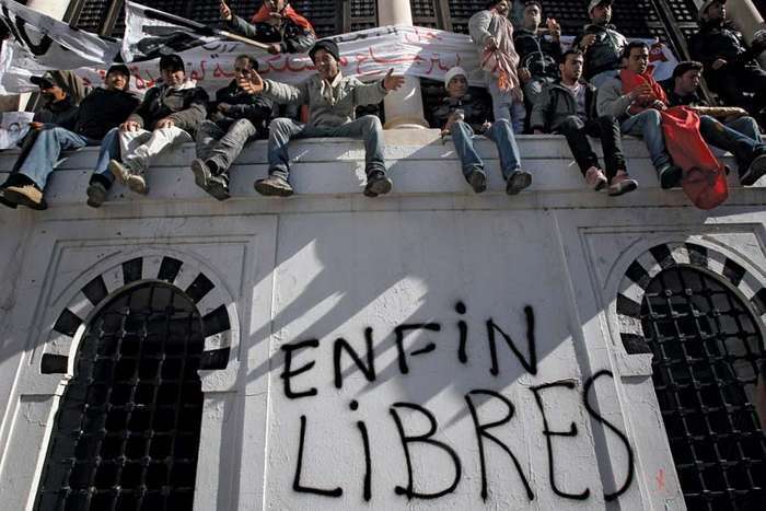 Demonstrators in the capital city of Tunis sitting on a wall where “Free at last” was written after the popular unrest of the Jasmine Revolution forced Tunisian Pres. Zine al-Abidine Ben Ali to step down, January 2011 