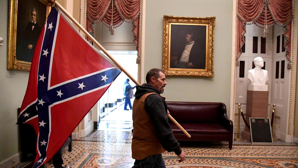 A Trump supporter carries a Confederate flag in the U.S. Capitol after a mob stormed the building, Jan. 6, 2021 