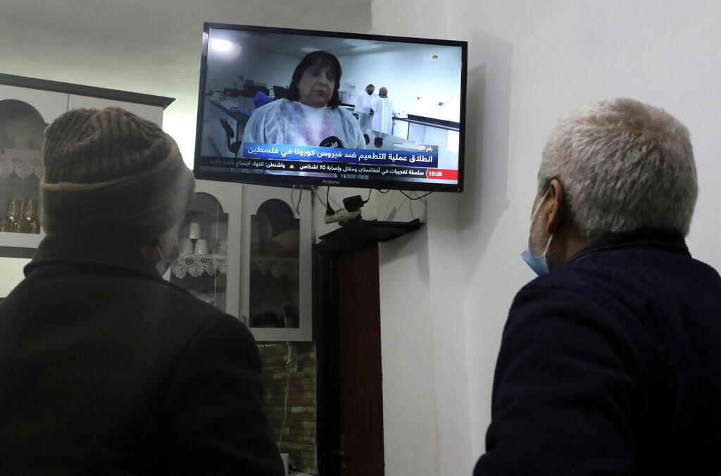 Palestinian men watch a live television broadcast of Palestinian Health Minister Mai al-Kaila announcing the start of vaccination against Covid-19, in the West Bank city of Hebron