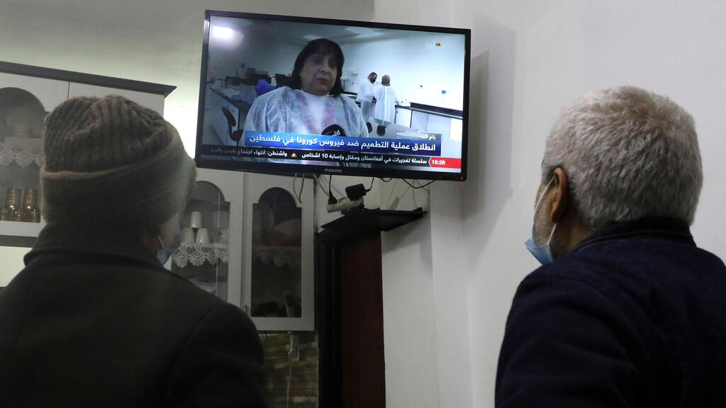 Palestinian men watch a live television broadcast of Palestinian Health Minister Mai al-Kaila announcing the start of vaccination against Covid-19, in the West Bank city of Hebron