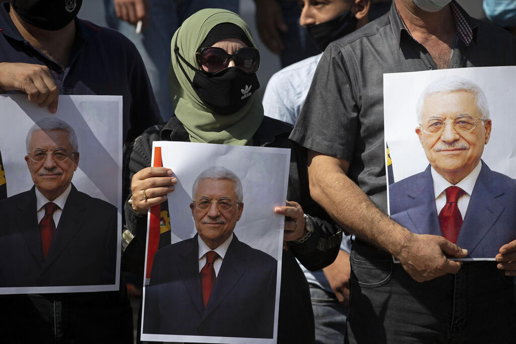 , Palestinians wearing protective face masks amid the coronavirus pandemic, hold pictures of Palestinian President Mahmoud Abbas during a rally to support Abbas