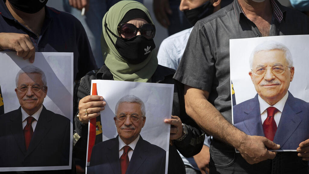 , Palestinians wearing protective face masks amid the coronavirus pandemic, hold pictures of Palestinian President Mahmoud Abbas during a rally to support Abbas