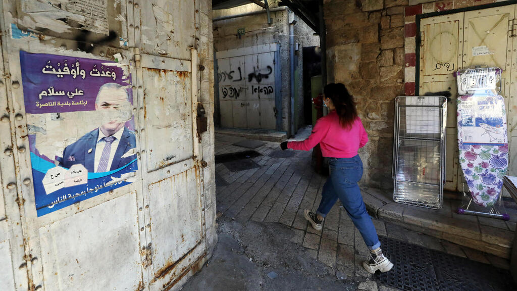 A woman walks past an old campaign poster depicting Ali Salam, the mayor of Nazareth, in the Old City of Nazareth 