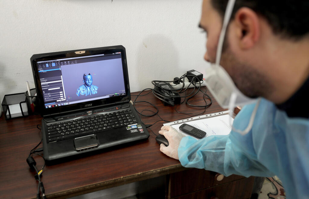 A physiotherapist works on a laptop as he designs 3D transparent face mask for Al-Deeb