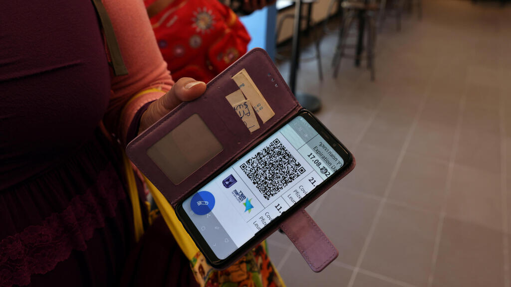 Israeli woman presents her Green Pass at entrance to a cafe (Photo: Reuters) התו הירוק בטלפון