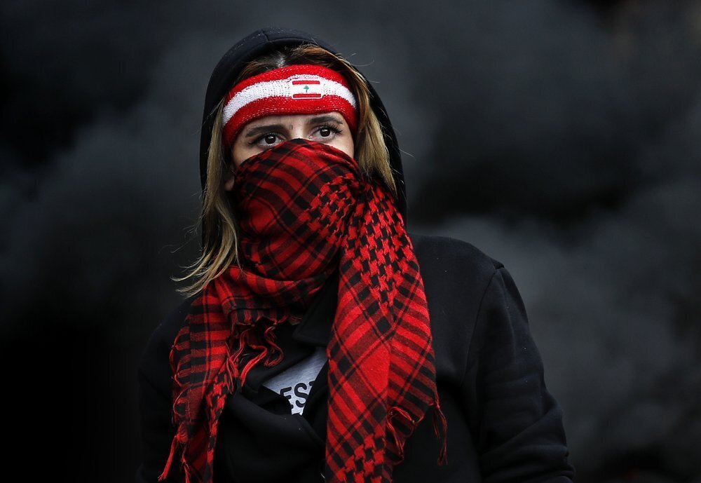 a protester covers her face with a scarf, as protesters block a main highway in the town of Zouk Mosbeh, north of Beirut, Lebanon 