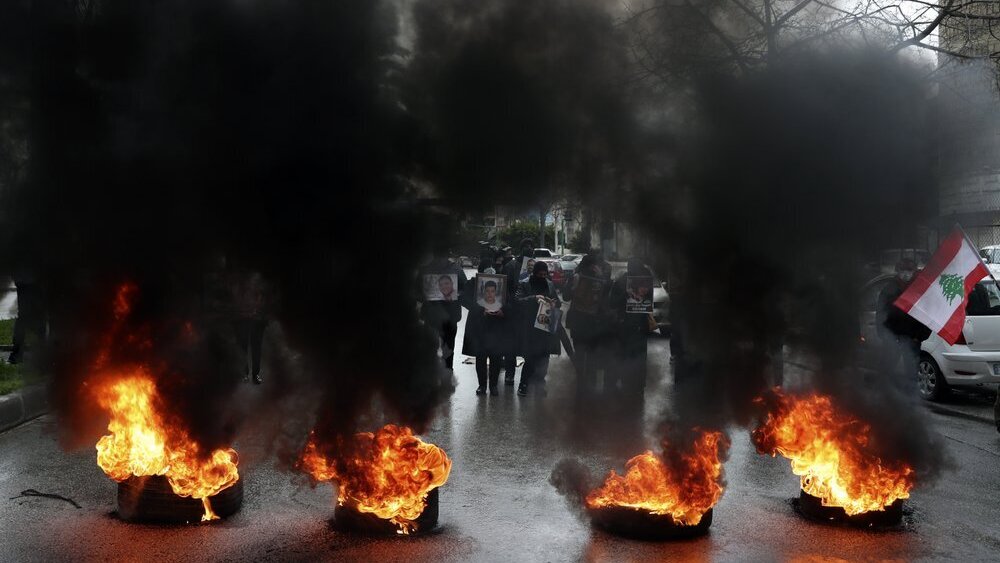 relatives of victims of the Aug. 4, 2020 Beirut port explosion hold portraits of their loved one who were killed, as they burn tires to block a road outside the Justice Palace, in Beirut, Lebanon 