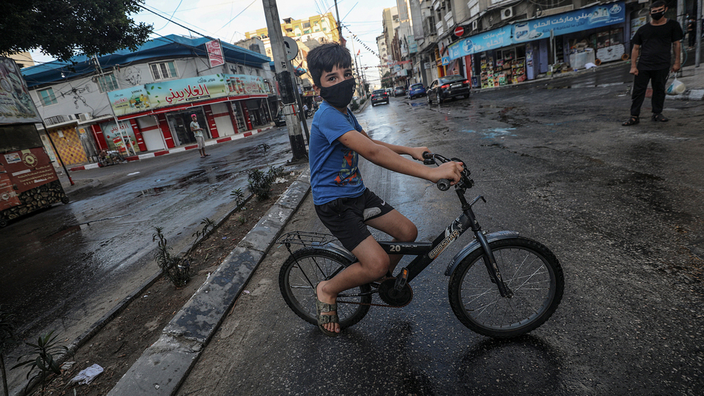 A boy wearing a facemask rides his bike on an empty Gaza street during the coronavirus lockdown 