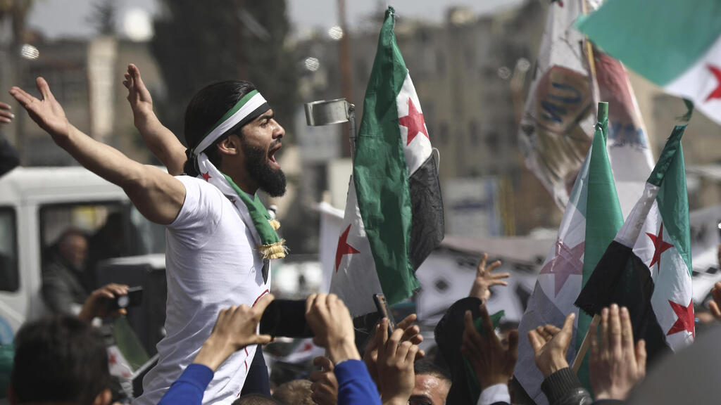 n anti-Syrian government protester shouts slogans as others wave revolutionary flags, to mark 10 years since the start of a popular uprising 