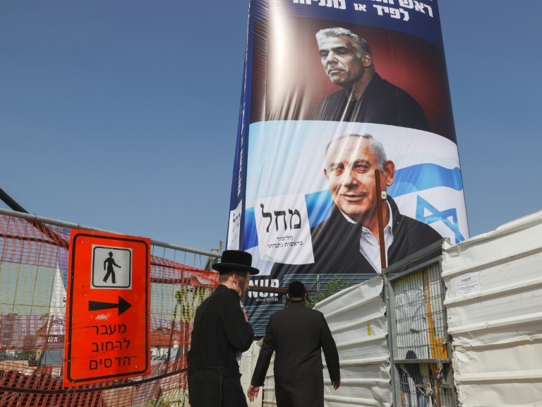 Ultra-Orthodox Jews walk past an election campaign poster bearing the image of opposition leader Yair Lapid (top) and Prime Minister Benjamin Netanyahu (bottom), in the central Israeli city of Bnei Brak 