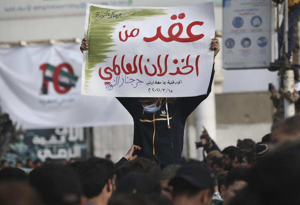 An anti-government protester holds up an Arabic placard that reads in part: "A decade of a global letdown 