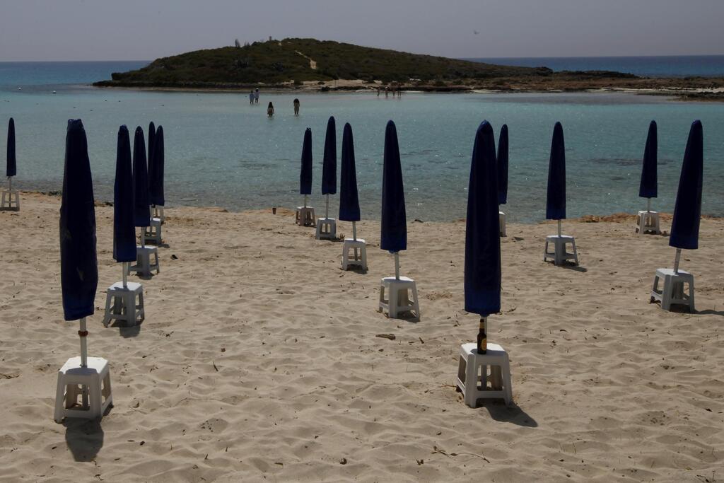 Rows of closed parasols on a nearly empty stretch of Nissi beach with a few beachgoers in the distance in Cyprus' seaside resort of Ayia Napa, a favorite among tourists from Europe and beyond 