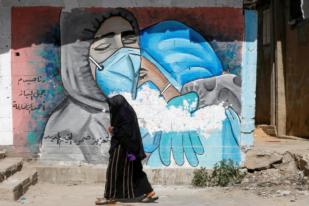 A Palestinian woman walks past a mural, amid the coronavirus disease (COVID-19) outbreak, in the central Gaza Strip 