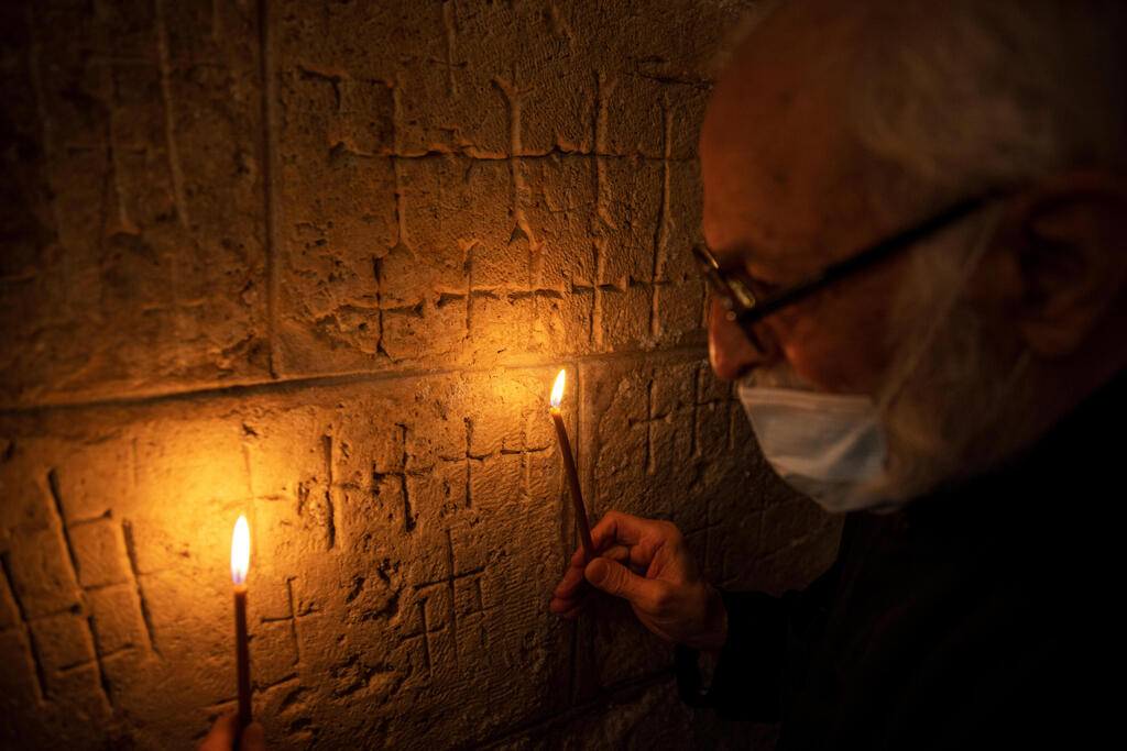 Father Samuel Aghoyan, the Armenian superior at the Church of the Holy Sepulchre holds candles to illuminate crosses etched into the ancient stone wall of the Saint Helena chapel inside the church 