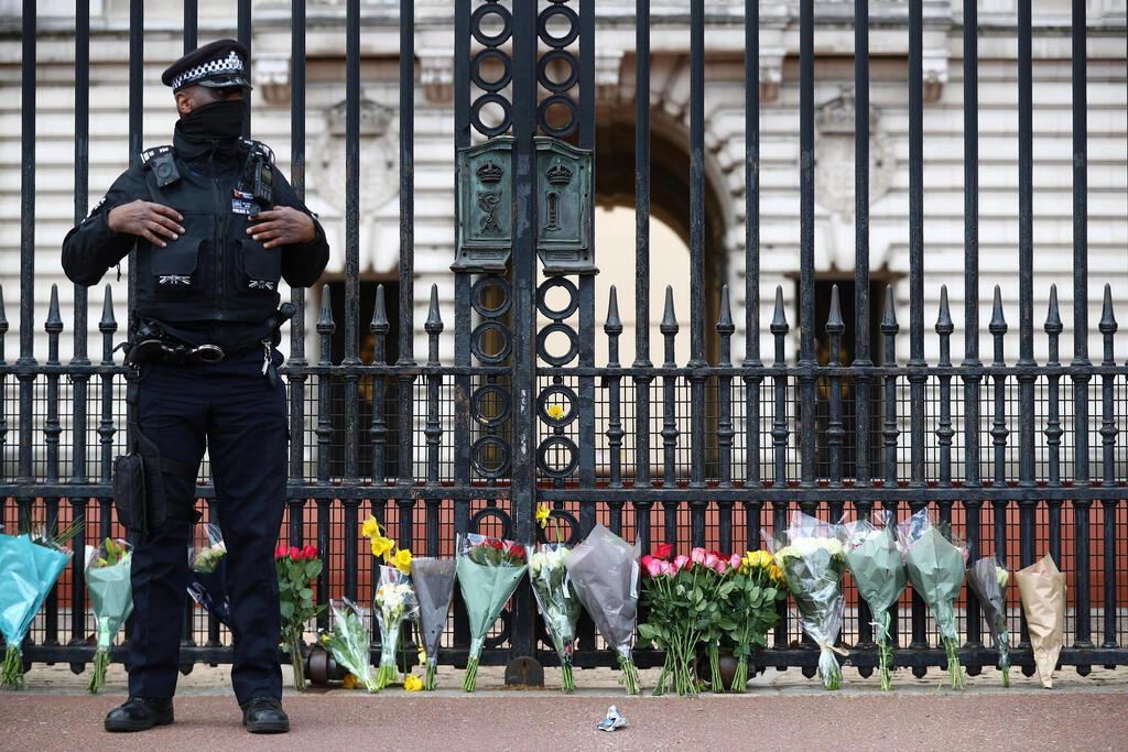A police officer stands next to bouquets of flowers outside Buckingham Palace in London after it was announced that Prince Philip, husband of Queen Elizabeth, has died at the age of 99, April 9, 2021 