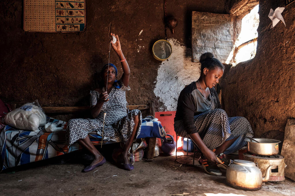 A woman member of the Ethiopian Jewish community works with a wool spool while another cooks at their home in the city of Gondar, Ethiopia 