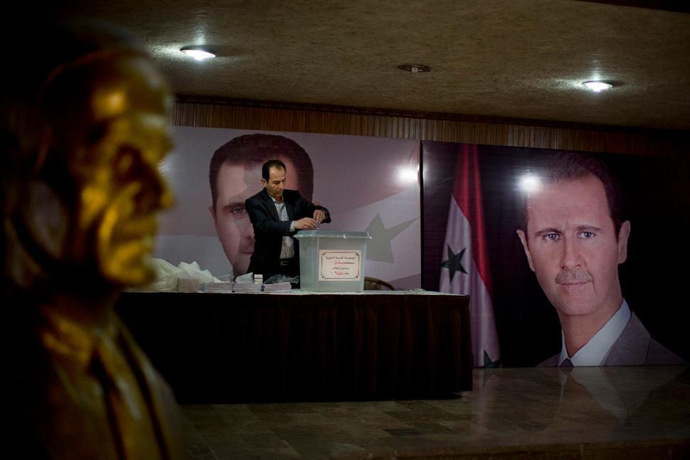 Syrian election official waits for voters at a polling station with posters of President Bashar Assad during the parliamentary election in Damascus, Syria, April 13, 2016