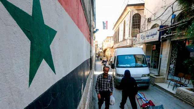 Man walks past mural of Syrian flag in Damascus
