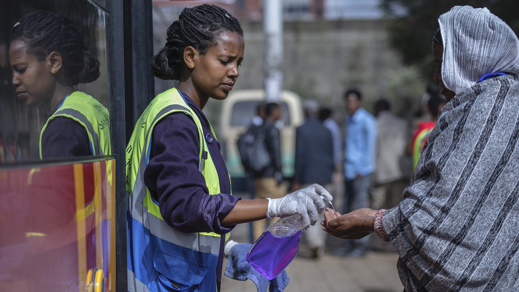 A volunteer provides hand sanitizer to passengers entering a bus as a precaution against the spread of the new coronavirus in the capital Addis Ababa, Ethiopia