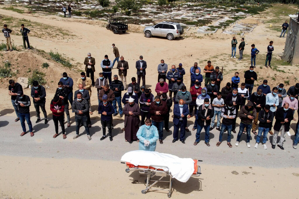 A picture taken with a drone shows Palestinians praying next to the body of a man, who died after contracting the coronavirus disease (COVID-19), before burial at a cemetery in the central Gaza Strip 