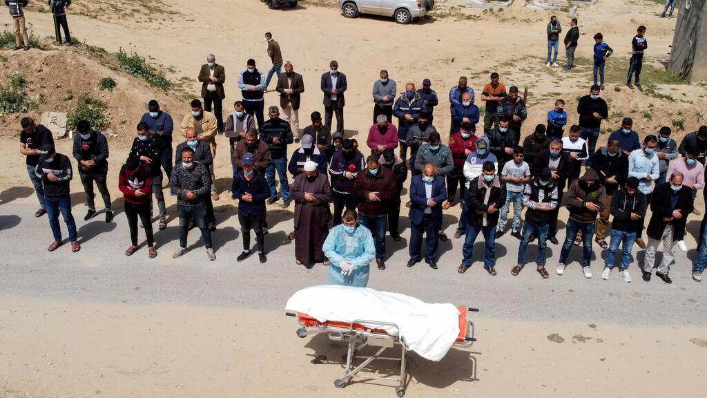 A picture taken with a drone shows Palestinians praying next to the body of a man, who died after contracting the coronavirus disease (COVID-19), before burial at a cemetery in the central Gaza Strip 