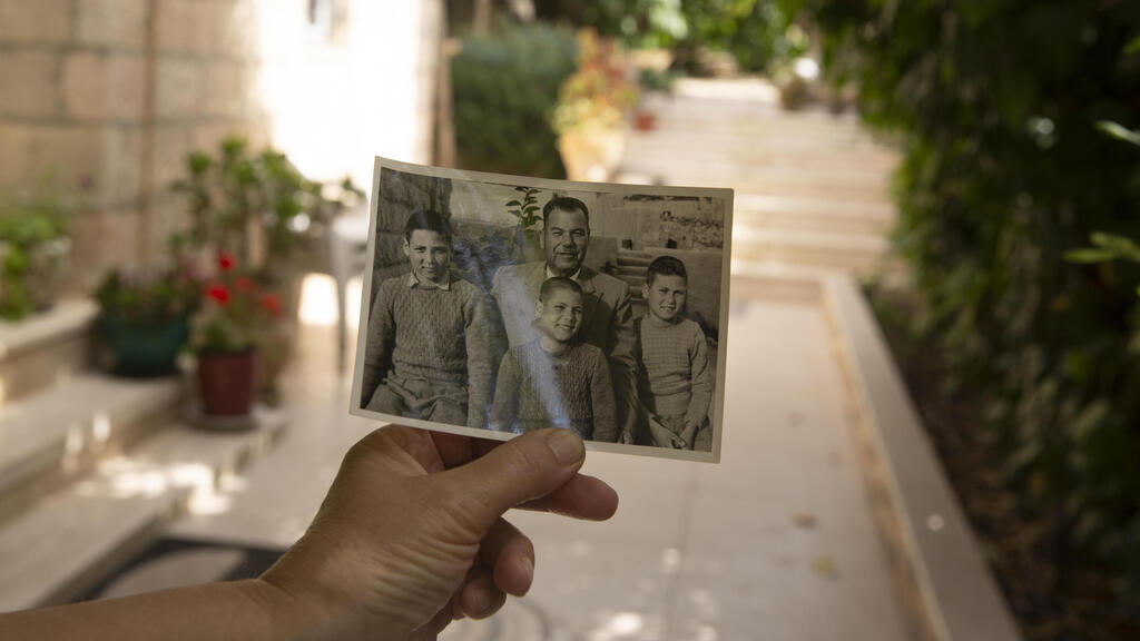 Samira Dajani holds a photo of her father, Fouad Moussa Dajani and his sons, taken in the same place in the courtyard of their home in the Sheikh Jarrah neighborhood  